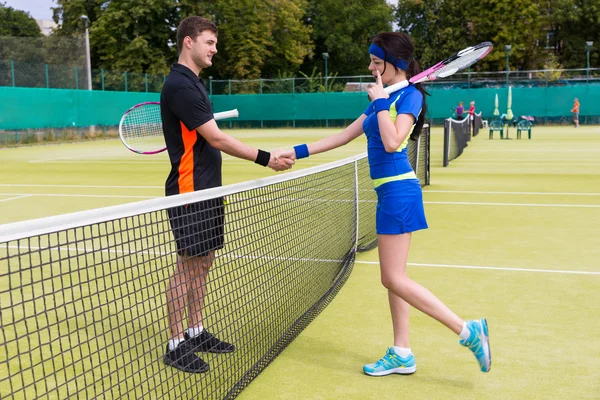 Jugadores de tenis masculinos y femeninos estrechando las manos sobre la red — Foto de Stock