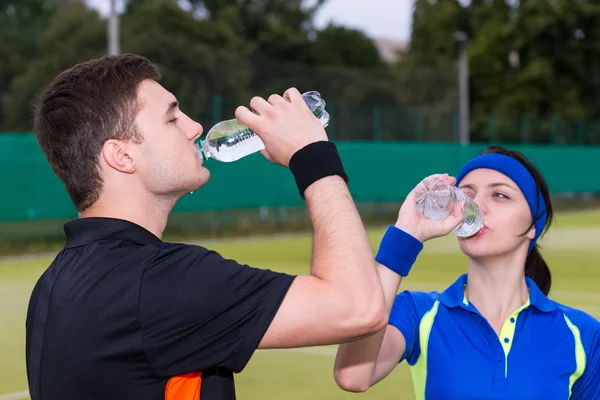 Athletic couple of tennis players drinking water after match out — Stock Photo, Image
