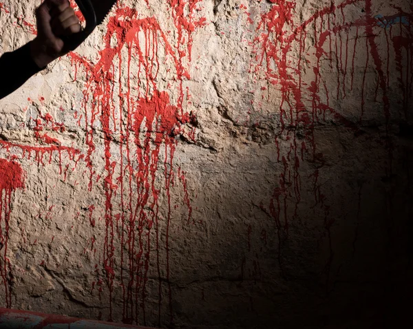 Parede manchada de sangue e mão masculina segurando uma serra — Fotografia de Stock