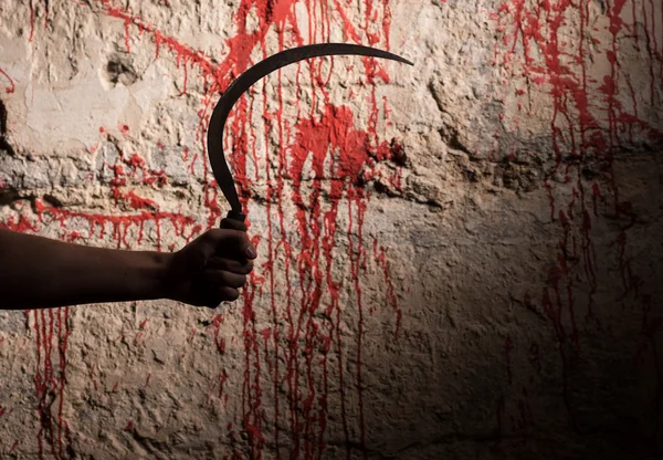 Mão masculina segurando uma foice na frente da parede manchada de sangue — Fotografia de Stock