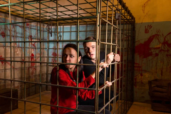 Couple of Halloween victims imprisoned in a metal cage looking o — Stock Photo, Image