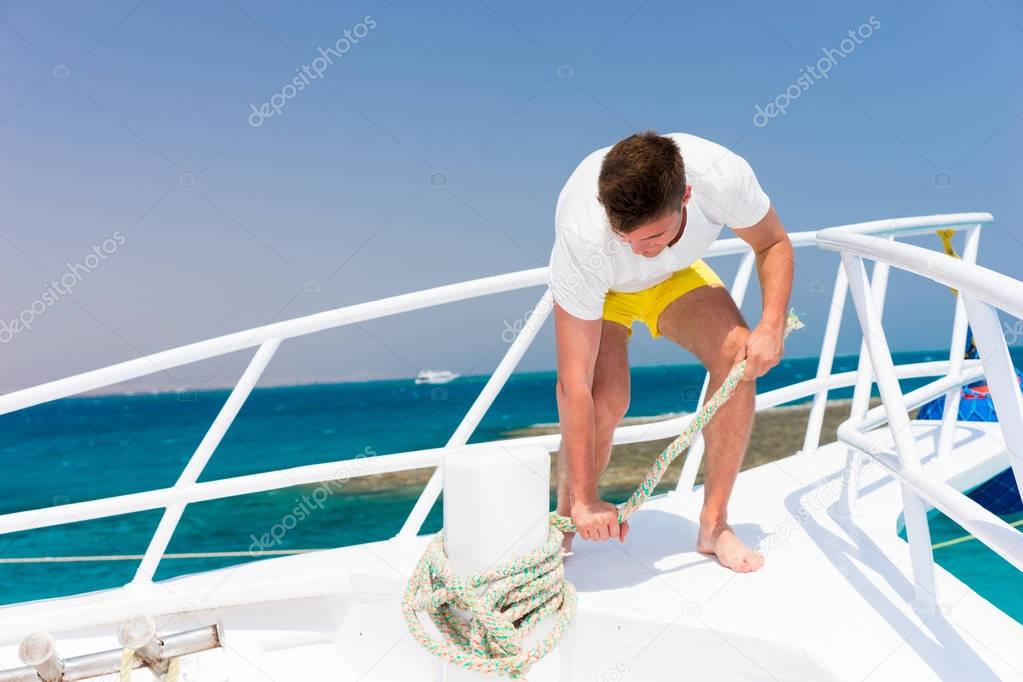 Young handsome man fixes rope on yacht at a sunny summer day