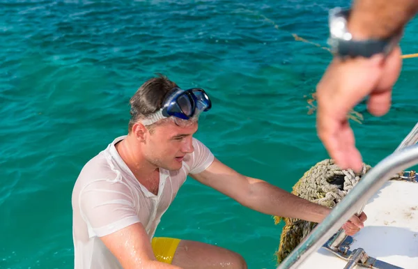 Jovem sobe para o barco após o mergulho — Fotografia de Stock