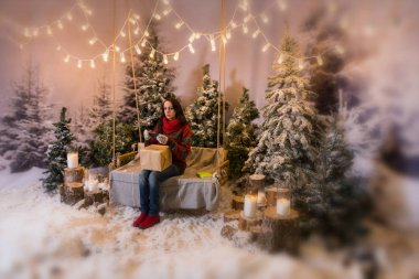 Kadın bir hediye ile bir salıncak üzerinde oturan ve mobil fon tutan