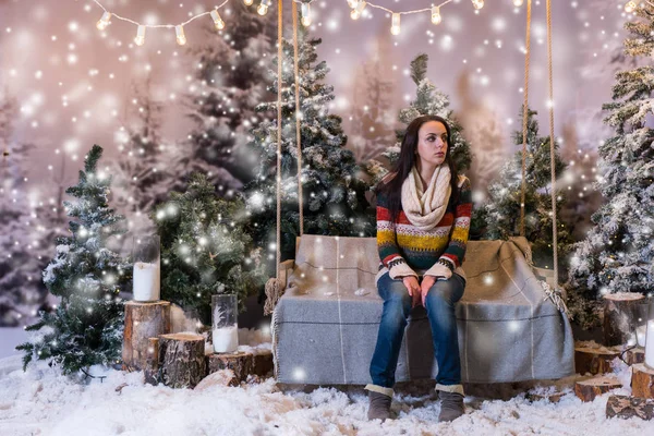 Young beautiful girl sitting on a bench or a swing in a snow-cov