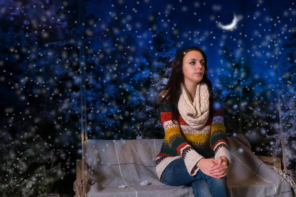 Chica joven sentada en un banco o un columpio en la noche en un sno — Foto de Stock