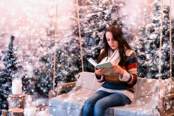 Mujer joven leyendo un libro mientras está sentada en un columpio con un blanco — Foto de Stock