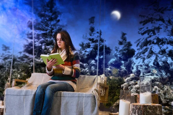 年轻女子坐在秋千上的一片空白的同时阅读一本书 — 图库照片