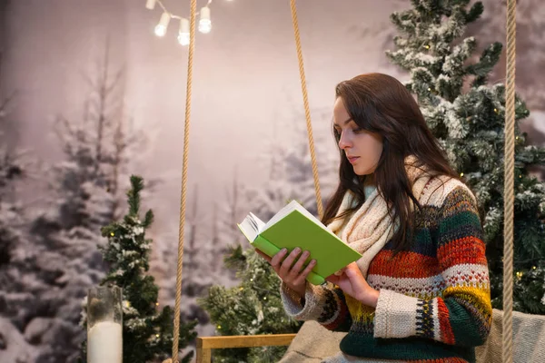 Romantic young woman reading a book while sitting on a swing wit — Stock Photo, Image