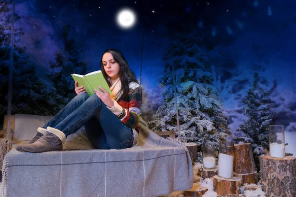 Genç kadın bacağı ile bir salıncak üzerinde otururken bir kitap okuma — Stok fotoğraf