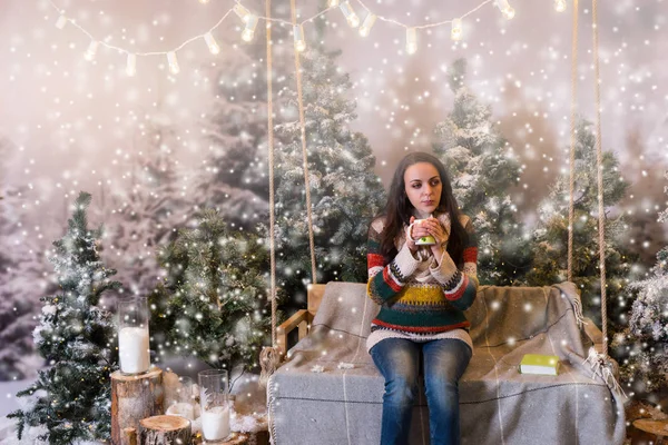 Cute female sitting on a swing with a blanket under the flashlig — Stock Photo, Image