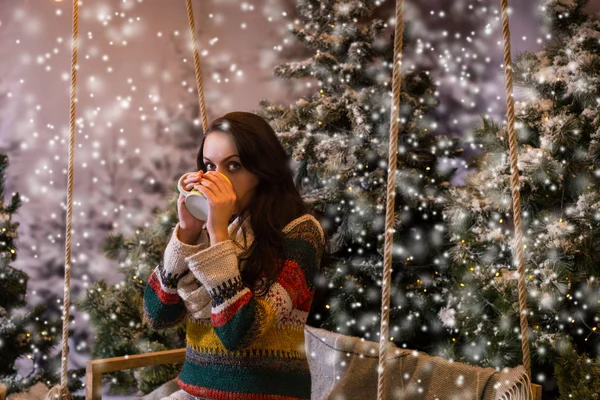 Jeune femme assise sur une balançoire et buvant une boisson chaude dans une tasse — Photo