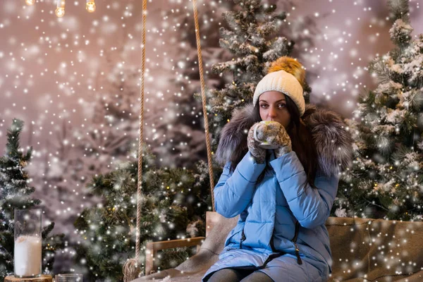 Female in blue down jacket drinking hot drink while sitting on a — Stock Photo, Image