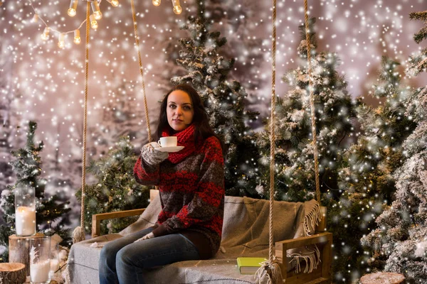 Young woman sitting on a swing with a blanket under the flashlig — Stock Photo, Image