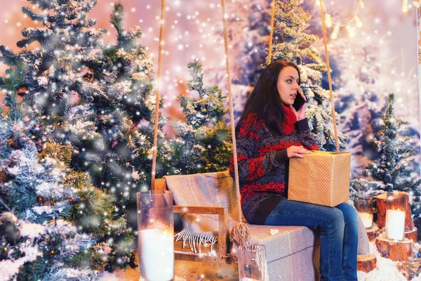 Jonge aantrekkelijke vrouw zitten op een schommel met een cadeautje en tal — Stockfoto