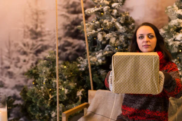 Woman sitting on a swing and offering a box with a present in a — Stock Photo, Image