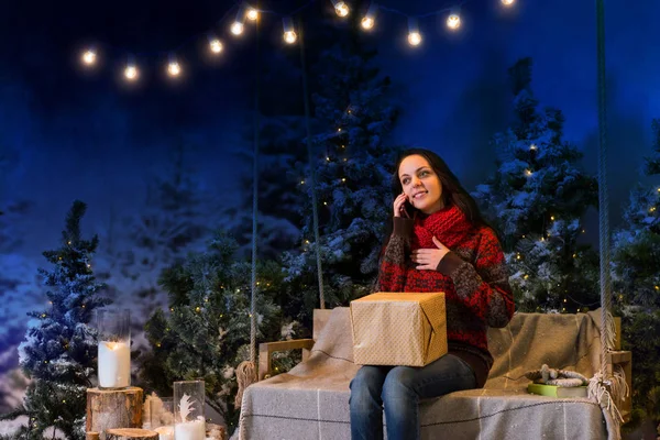 Mujer feliz sentada en un columpio con un regalo y hablando en el — Foto de Stock