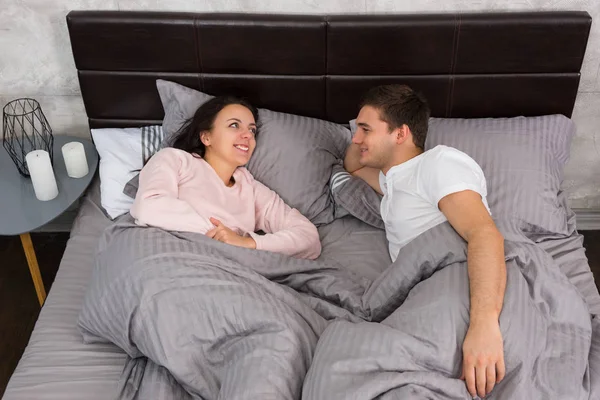 Casal jovem conversando enquanto deitado na cama e vestindo pijama — Fotografia de Stock