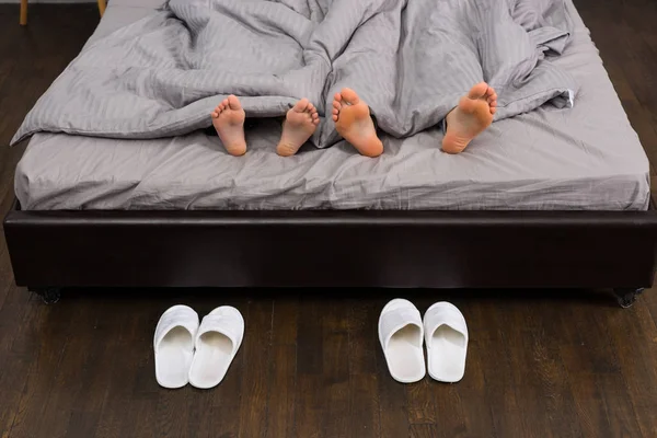 Close up of male and female feet under grey blanket, near two pa — Stock Photo, Image