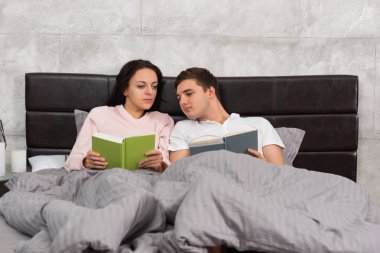 Genç çift birbirlerine yatakta yatarken kitap okuma ve