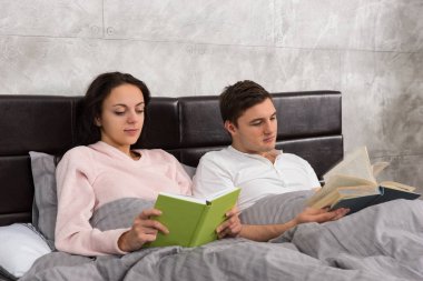 Genç mutlu çift yatakta yatan ve nedir kitap okuma