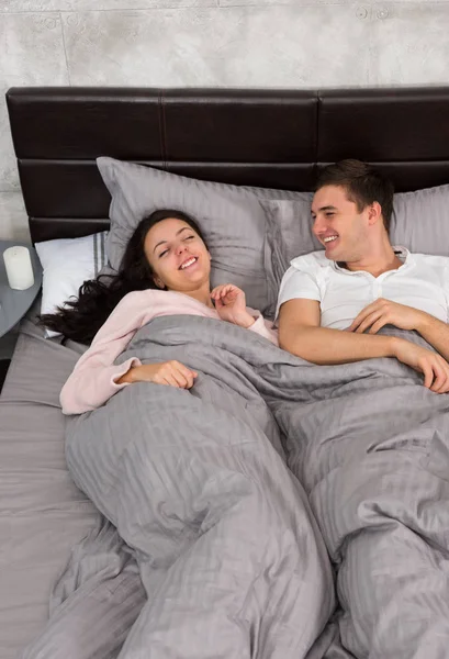 Casal jovem rindo e vestindo pijama enquanto deitado na cama — Fotografia de Stock