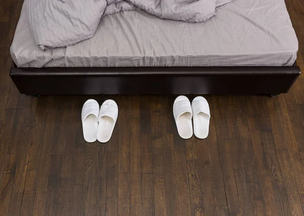 Domestic white slippers are beside the bed — Stock Photo, Image