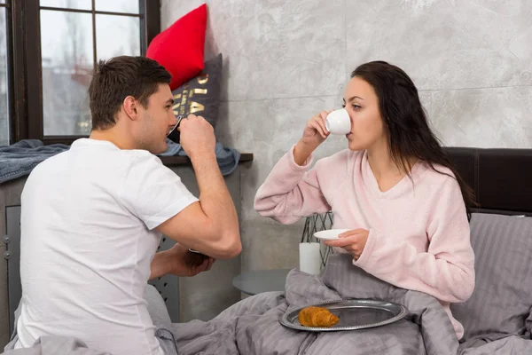 Unga lyckliga paret vaknade precis, dricka en kopp kaffe och ha br — Stockfoto