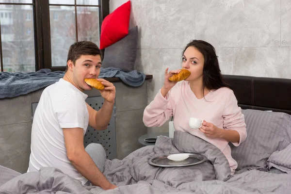 Mladý šťastný pár právě probudil, jídlo croissanty a mají brea — Stock fotografie