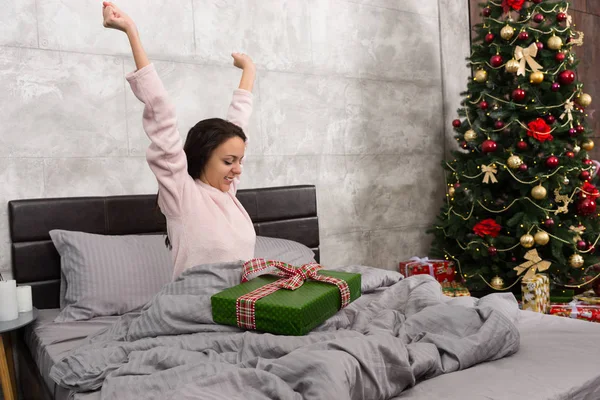 Šťastná mladá žena probudí a radovat se v její současné w vánoční — Stock fotografie