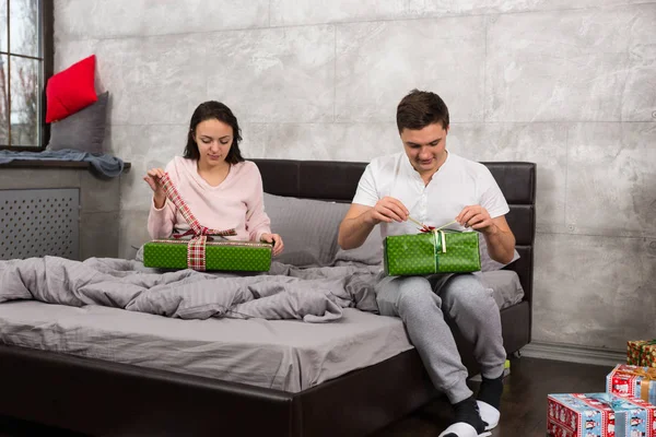 Young pair in pajamas unpacking their presents while sitting on — Stock Photo, Image