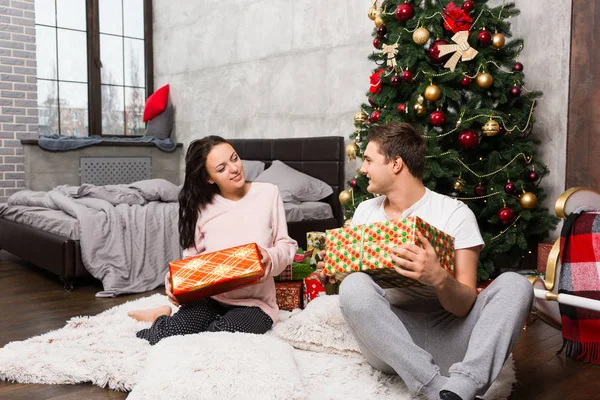 Jovem casal de pijama se alegrar com seus presentes enquanto sentado — Fotografia de Stock