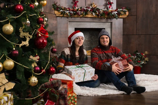 Šťastný pár a vtipné zimní čepice hospodářství dary při sezení o — Stock fotografie