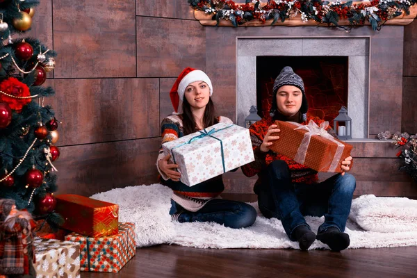 Jovem casal em camisolas quentes e chapéus de inverno engraçados dando prese — Fotografia de Stock