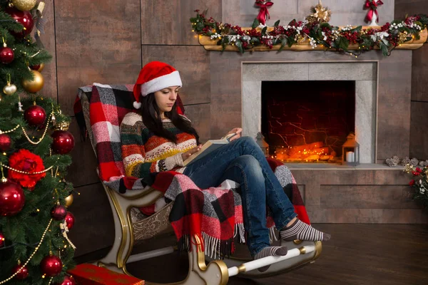 Joven mujer concentrada en divertido sombrero de Navidad lectura mientras si —  Fotos de Stock