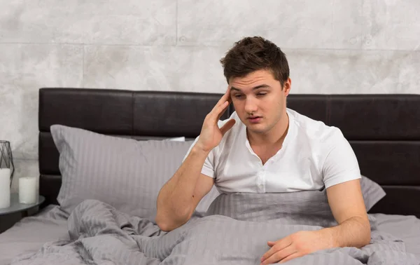Young man woke up with hangover sitting in stylish bed with grey
