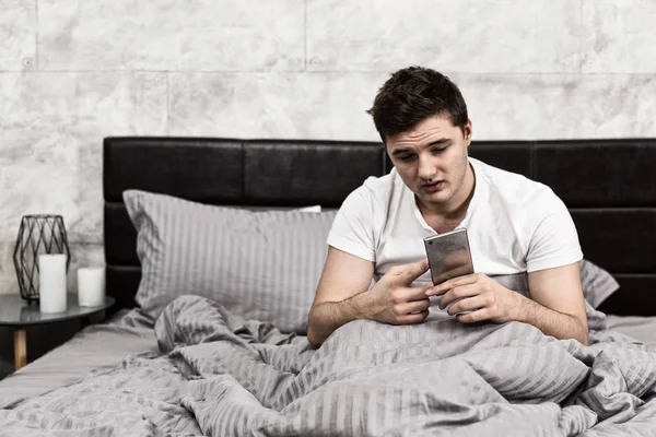 Jonge moe man kijkend naar zijn mobiele telefoon zittend in stal — Stockfoto