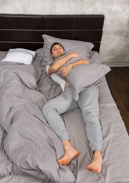 Bonito homem cansado no pijama dormindo sozinho sem cobertor e — Fotografia de Stock