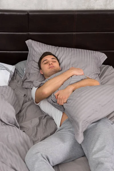 Bonito jovem cansado no pijama dormindo sozinho sem cobertor — Fotografia de Stock