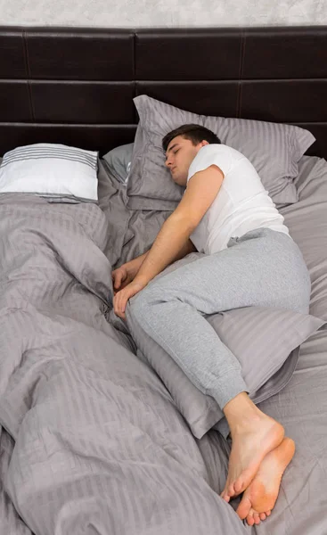 Hermoso hombre cansado en pijama durmiendo solo sin manta en —  Fotos de Stock