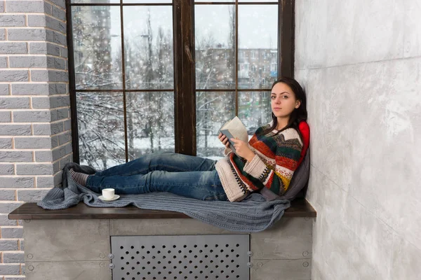 Young beautiful woman lying on the windowsill and looking at the — Stock Photo, Image