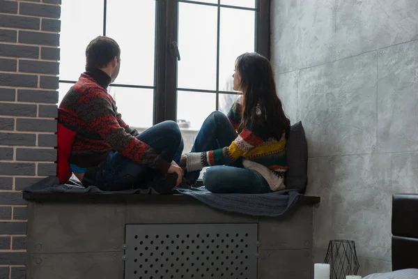 Молодая пара в теплых трикотажных свитерах, выглядывающая в окно. — стоковое фото