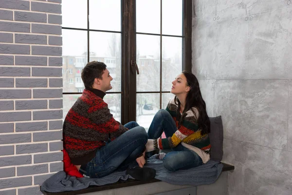 Young pair in warm knitted sweaters talking while sitting on the — Stock Photo, Image
