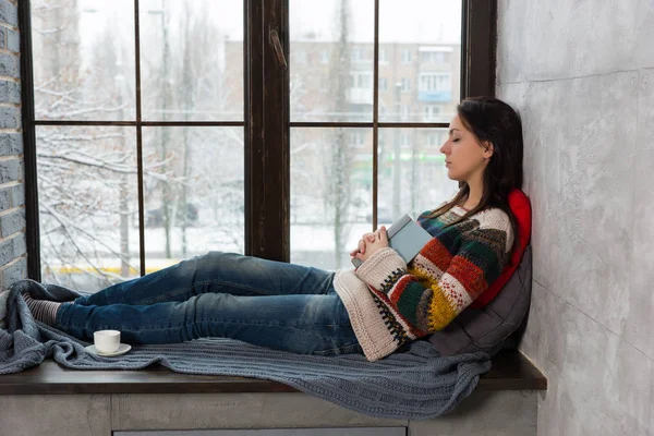 年轻有魅力的女人睡在阅读时的窗台上 — 图库照片
