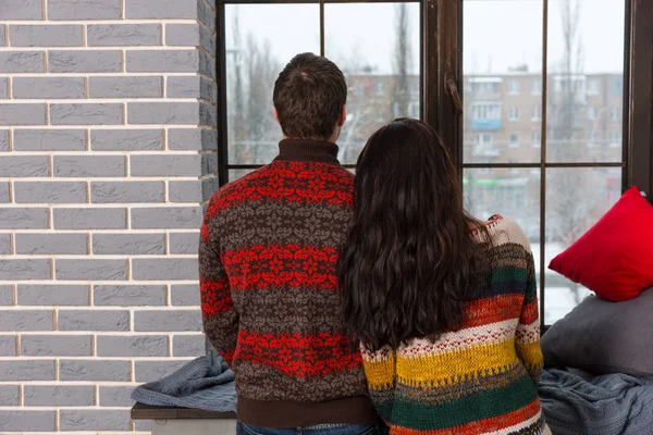 Jonge paar in warme gebreide truien kijkt uit het raam terwijl — Stockfoto