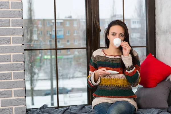 Młoda kobieta pije kawę siedząc na parapecie — Zdjęcie stockowe