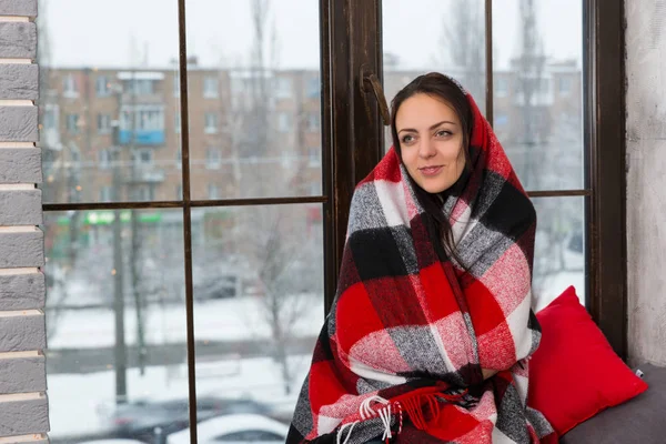 Jonge lachende vrouw gewikkeld in een deken zittend op het wi — Stockfoto