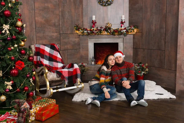 Dulce pareja sentada en una alfombra frente a la chimenea decorada —  Fotos de Stock