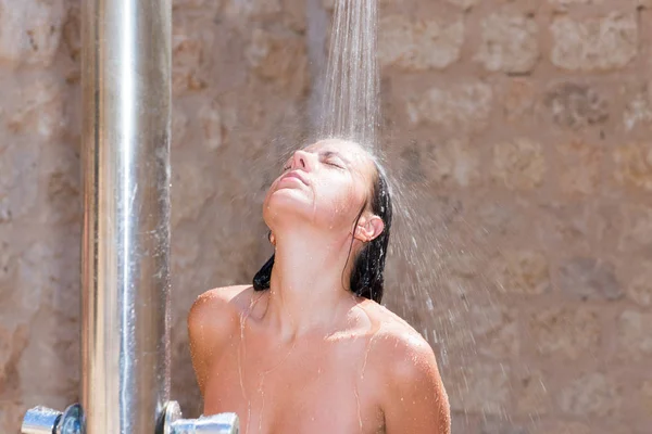 Atractiva joven hembra de pie bajo la ducha de la piscina al aire libre a — Foto de Stock