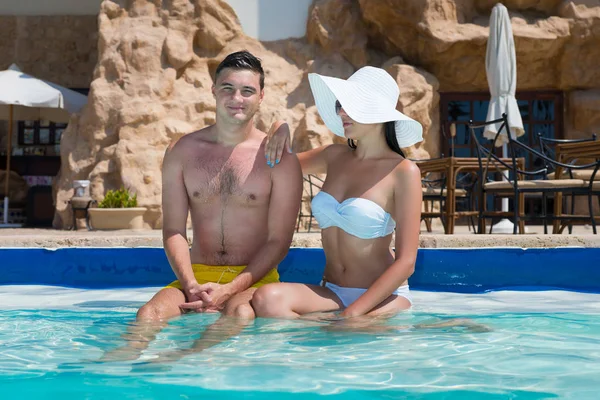 Happy young couple sitting on the edge of swimming pool — Stock Photo, Image